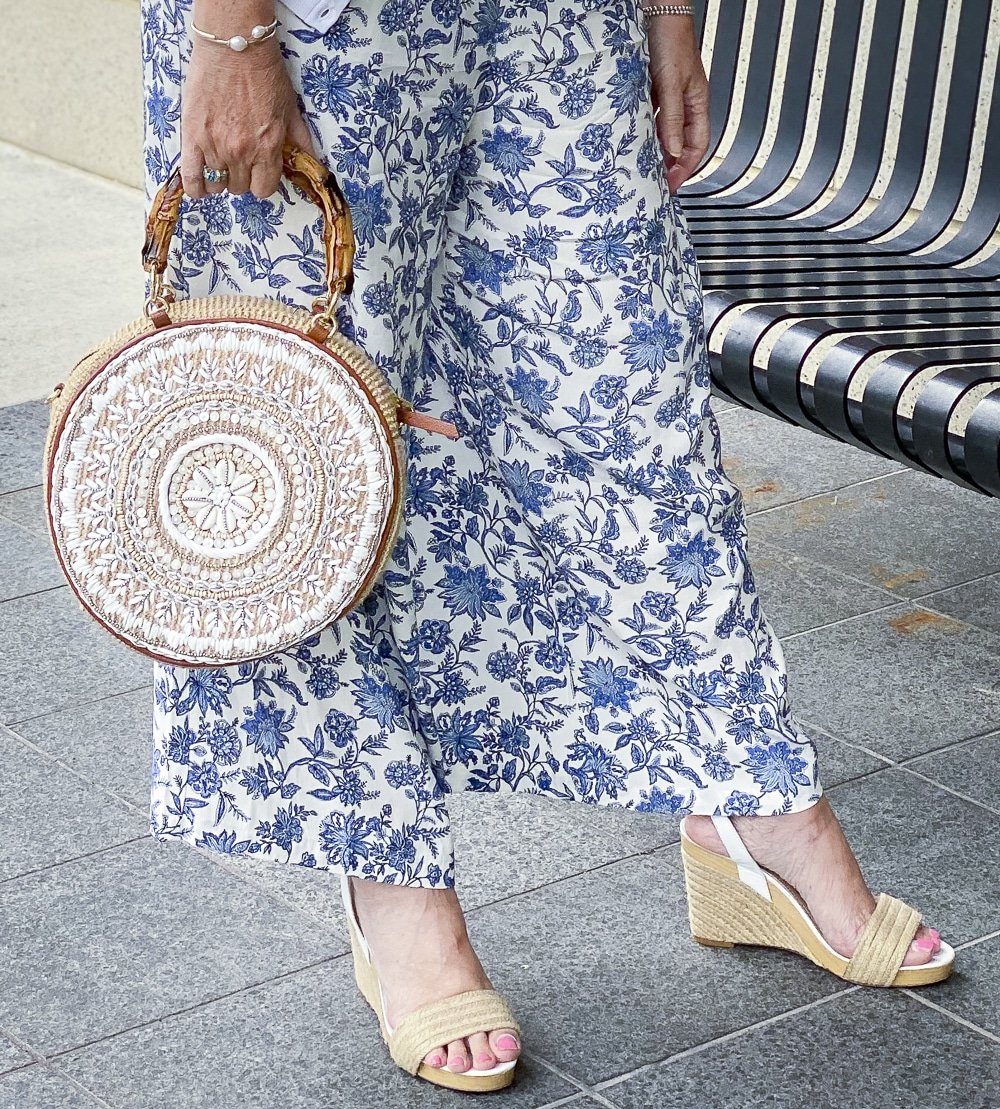 Fashion Blogger 50 Is Not Old is wearing a blue and white jumpsuit from Loft with white espadrille wedge sandals and a beaded circle handbag from Chico's