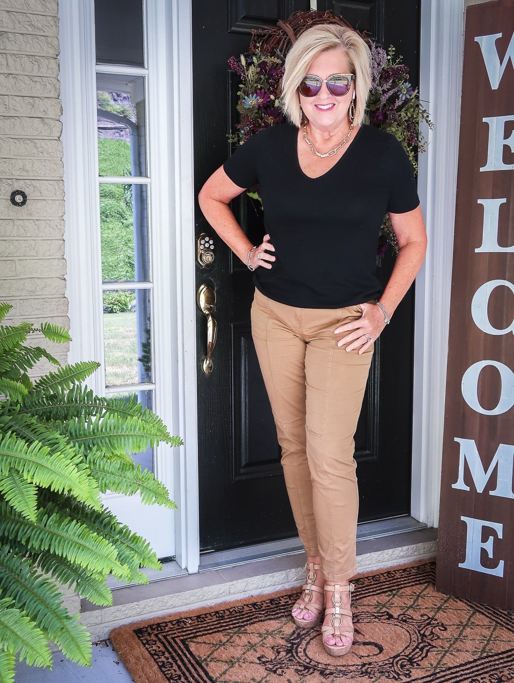 Fashion Blogger 50 Is Not Old is wearing a black v-neck t-shirt, camel colored utility pants, and gold link statement jewelry