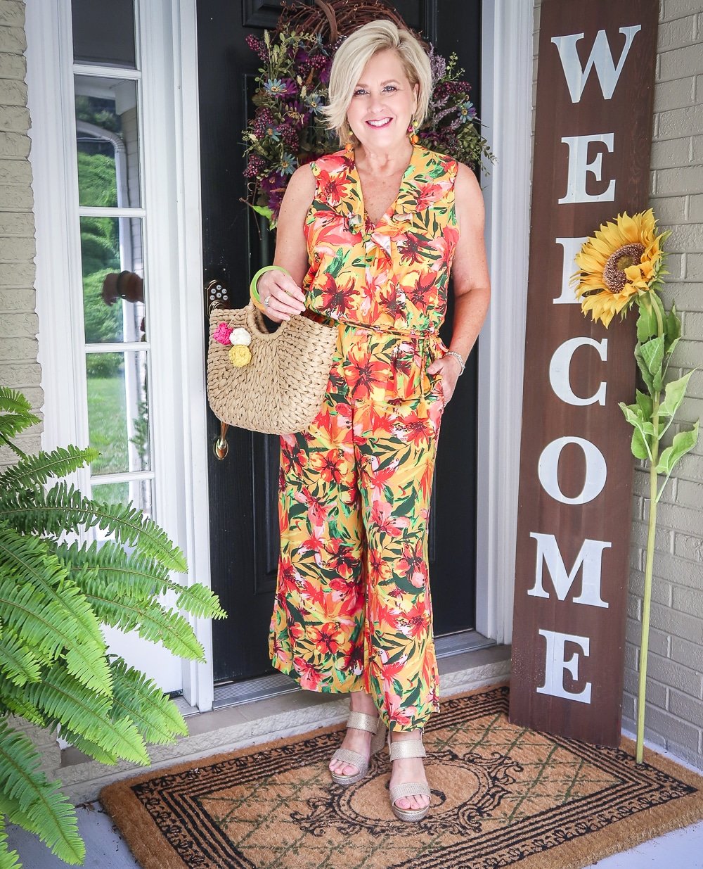 Fashion Blogger 50 Is Not Old is wearing a tropical ruffled peplum top, and a matching pant with gold espadrille wedges and a straw bag