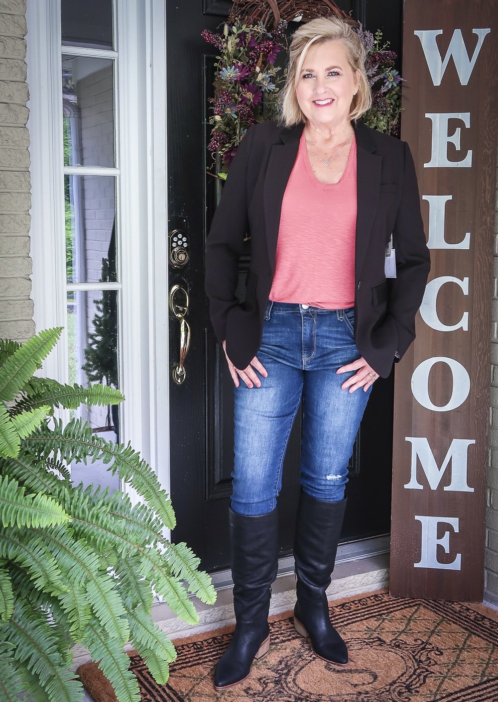 Fashion Blogger 50 Is Not Old is wearing a red v-neck t-shirt, a black blazer, a pair of distressed jeans and black knee boots