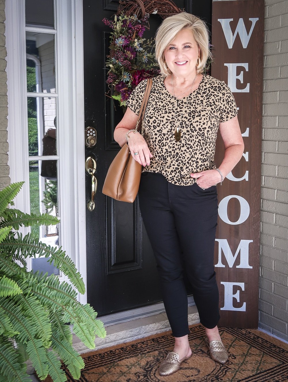 Fashion Blogger 50 Is Not Old is wearing a v-neck leopard tee, black girlfriend jeans, gold mules, and carrying a brown tote