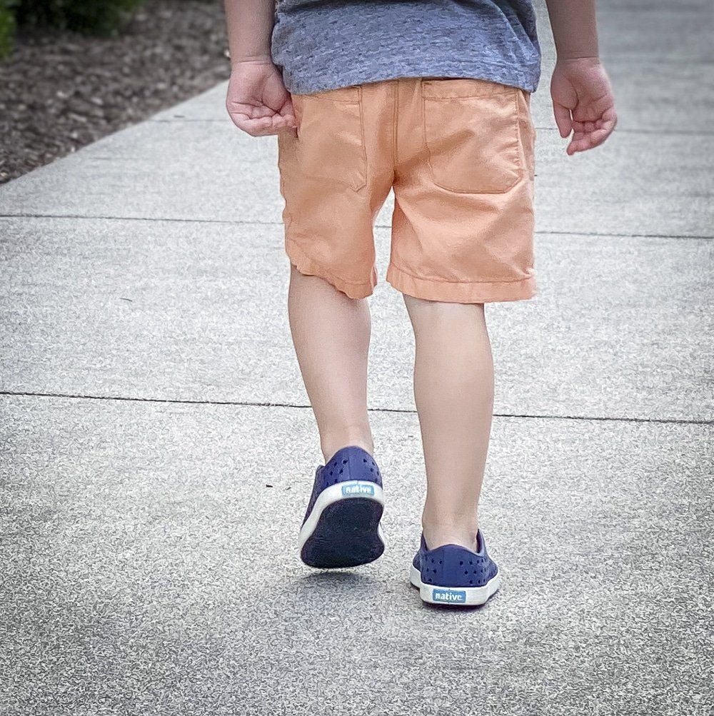 Fashion Blogger 50 Is Not Old's grandchildren in their back to school outfits. He is wearing orange shorts from Carters, and navy blue Native sneakers