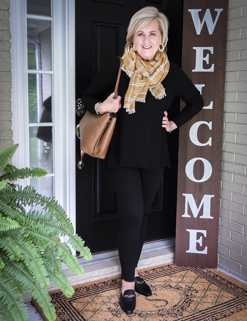 Fashion Blogger 50 Is Not Old is wearing a black tunic sweater, with a blanket scarf, black distressed jeans and black slides