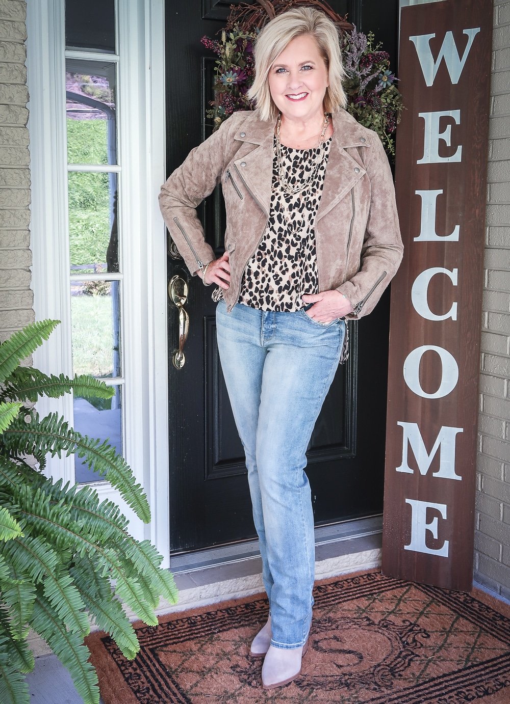 Fashion Blogger 50 Is Not Old is wearing a leopard print statement top, a taupe suede moto jacket, and a pair of straight leg jeans 