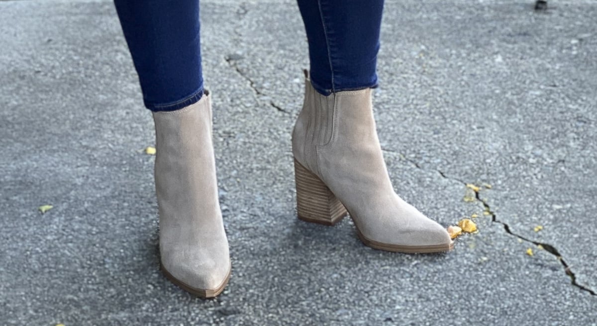 Fashion Blogger 50 Is Not Old is standing on a sidewalk in suede ankle boots