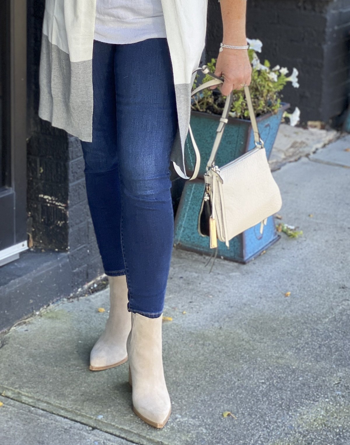 Fashion Blogger 50 Is Not Old is standing on a sidewalk in dark skinny jeans, suede ankle boots, and carrying a Vince Camuto crossbody handbag