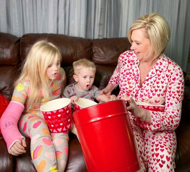 Fashion Blogger 50 Is Not Old is showing her grandchildren the huge red popcorn tin from the Popcorn Factory she purchased using her AARP member benefits