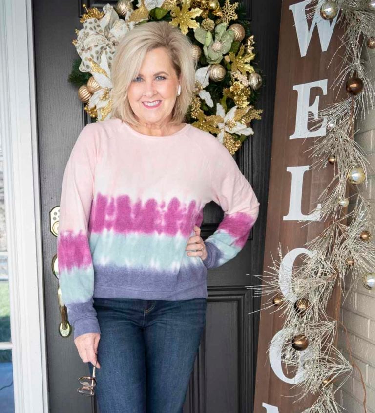 Over 40 Fashion Blogger 50 Is Not Old is wearing tie dye sweatshirt and holding a pair of blue light glasses