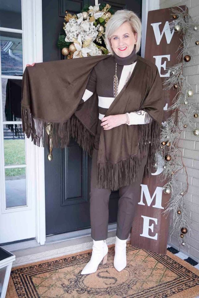 Fashion Blogger 50 Is Not Old is wearing a colorblocked turtleneck with ankle pants, and showing a fringed ruana