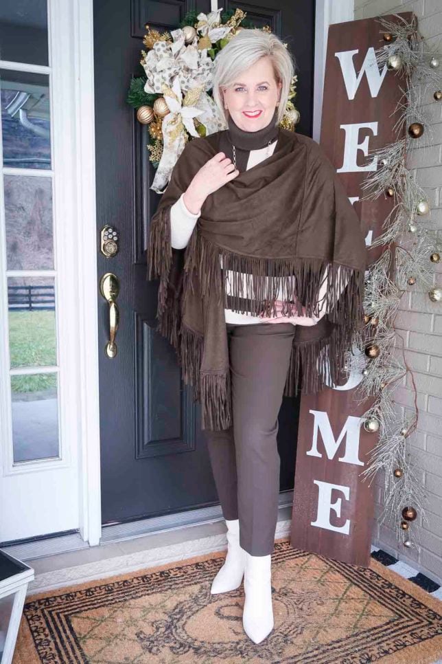 Fashion Blogger 50 Is Not Old is wearing a colorblocked turtleneck with ankle pants, wearing a fringed ruana as a wrap, and white ankle boots