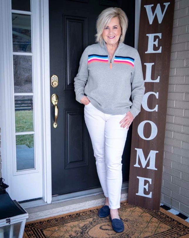 Fashion Blogger 50 Is Not Old is wearing a rainbow striped pullover sweater and white ankle jeans with navy flats