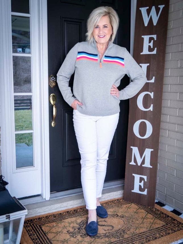 Fashion Blogger 50 Is Not Old is wearing a rainbow striped pullover sweater and white jeans with navy loafers