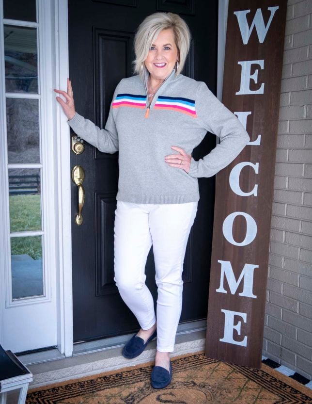 Fashion Blogger 50 Is Not Old is wearing a rainbow striped pullover sweater and white ankle jeans with navy loafers