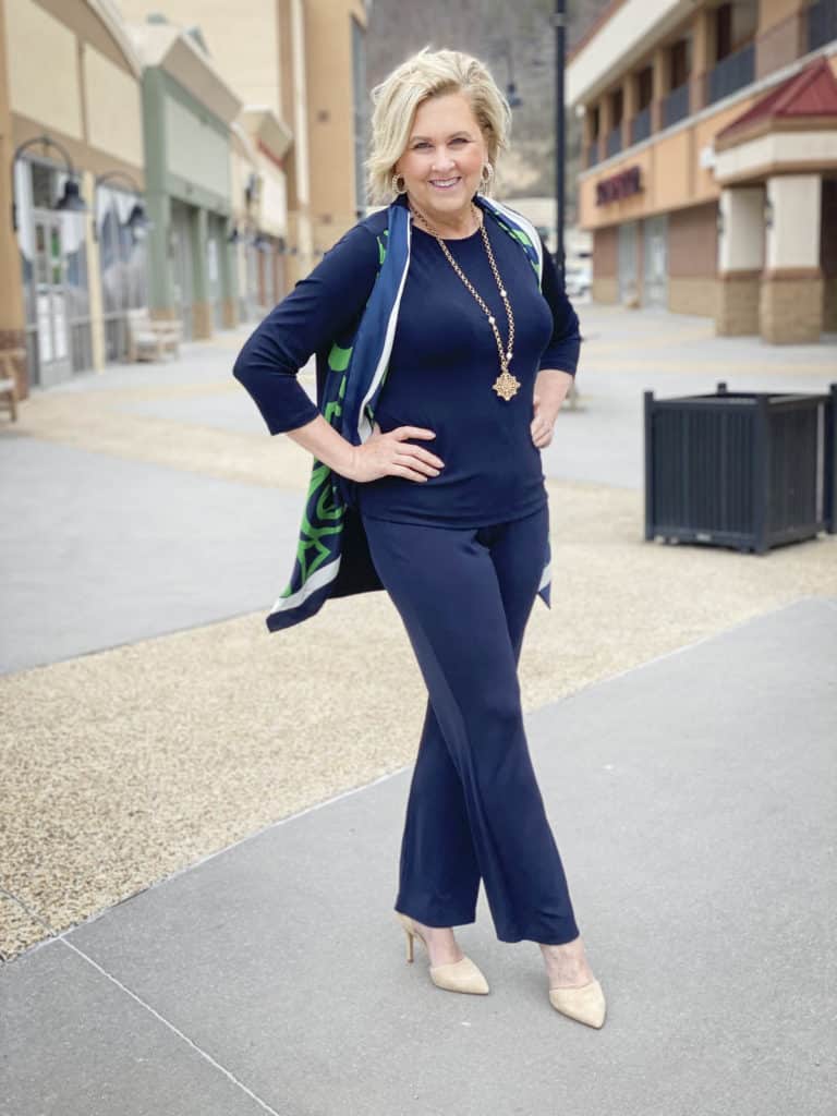 Fashion Blogger 50 Is Not Old is wearing a monochromatic navy outfit with a scarf cardigan, neutral shoes, and gold jewelry from Chico's