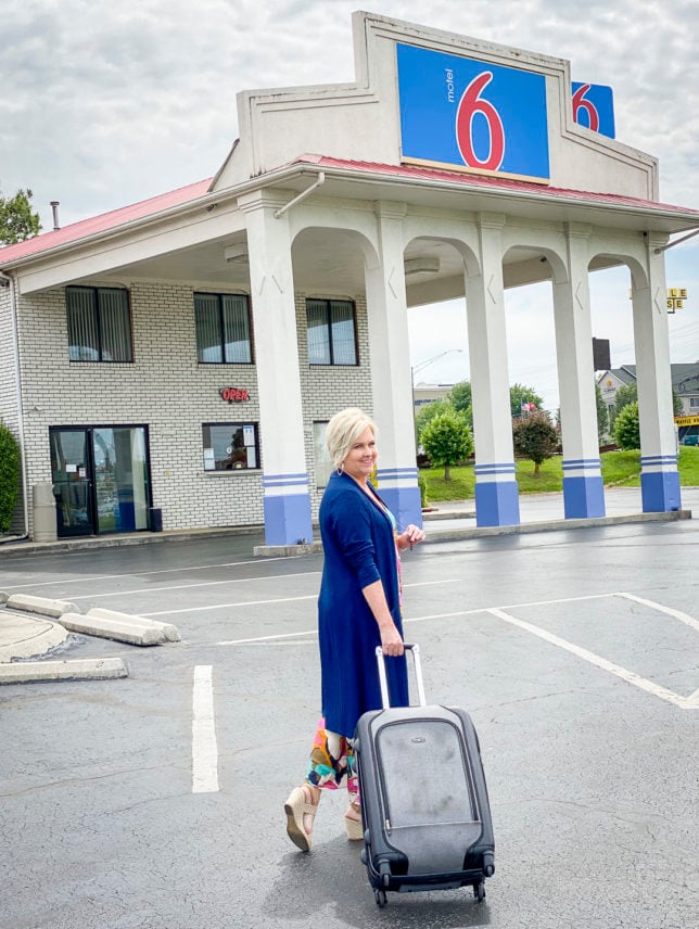 Fashion Blogger 50 Is Not Old is walking with her luggage toward a Motel 6