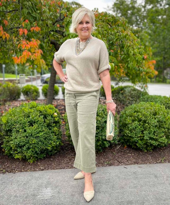 Fashion Blogger 50 Is Not Old is showing an example of wearing neutrals for the fall with an embellished beige sweater, olive crop pants, and neutral flats