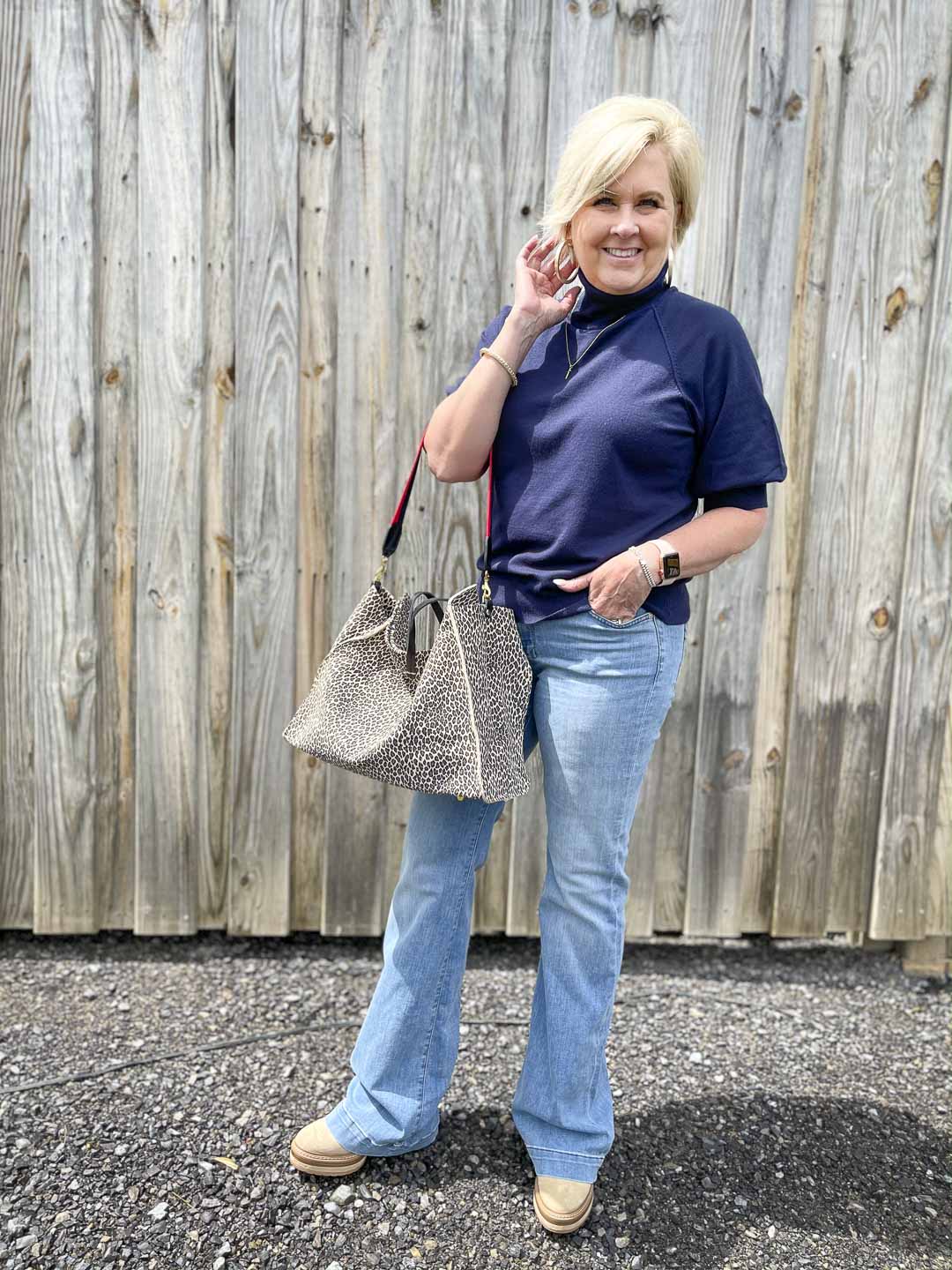 Over 40 Fashion Blogger, Tania Stephens, is wearing a navy turtleneck sweater, a pair of flare jeans, and carrying a large tote bag
