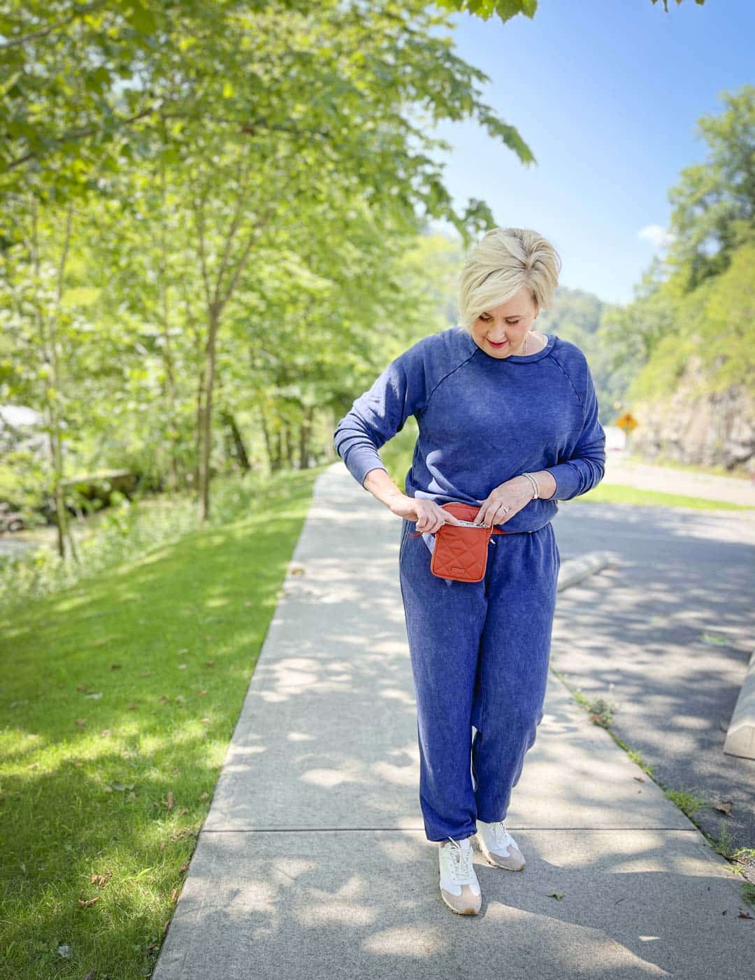 Over 40 Fashion Blogger, Tania Stephens, is wearing a navy sweatshirt and sweatpants set with Tory Burch sneakers and looking in her crossbody Terracotta bag from Vera Bradley