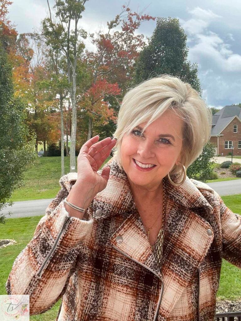 Over 40 fashion blogger, Tania Stephens is wearing a plaid moto jacket with trees in the background