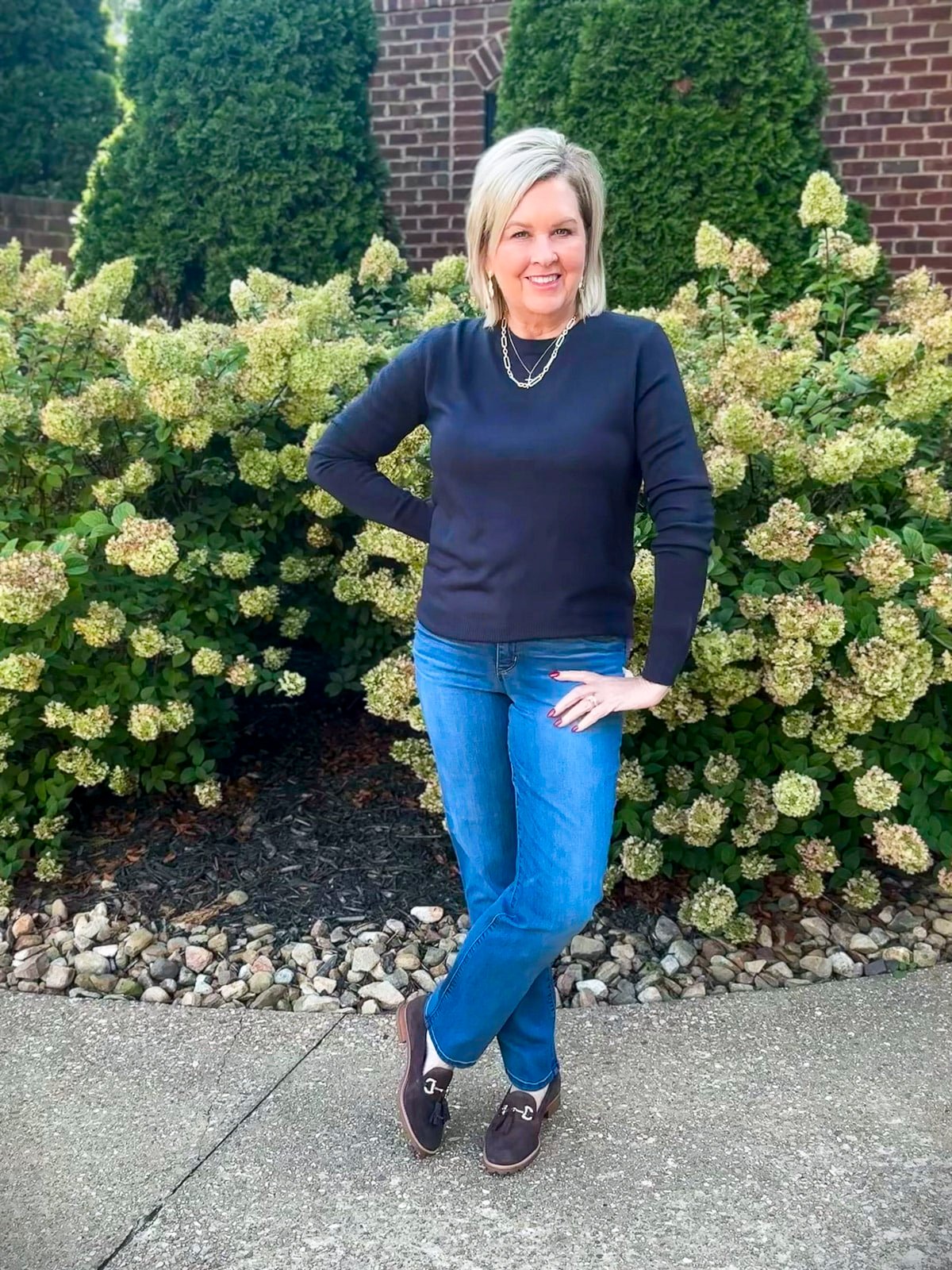 Fashion Blogger Tania Stephens is wearing a navy pullover sweater with jeans and brown loafers 