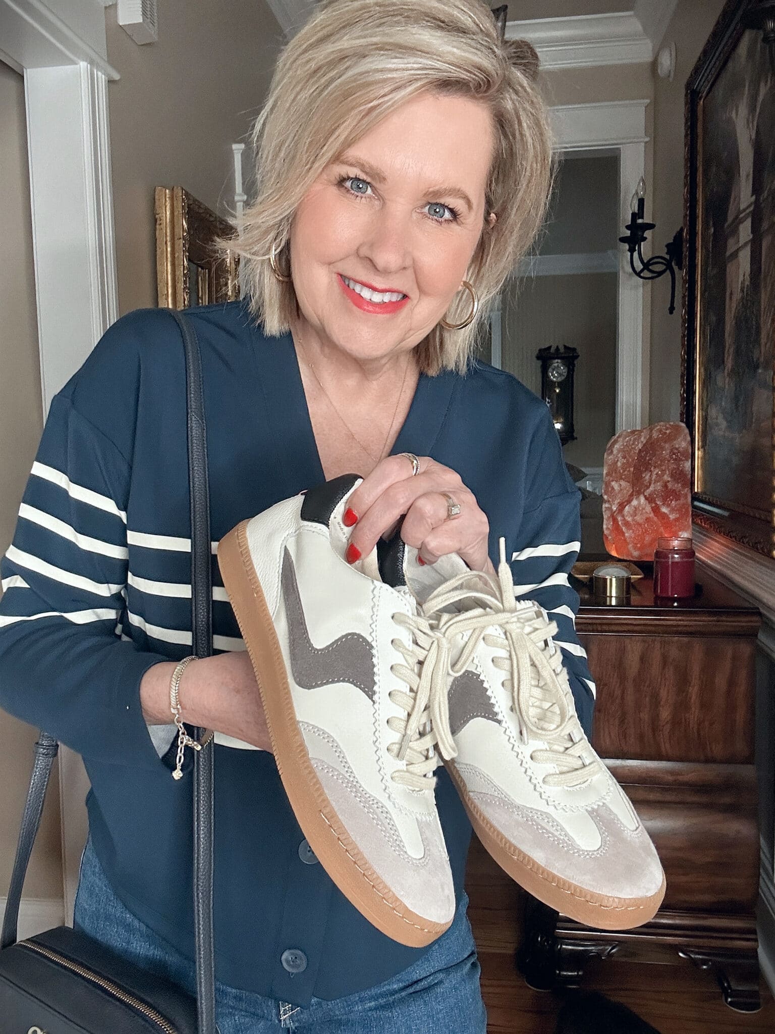 Over 50 Fashion Blogger, Tania Stephens, wearing a SPANX Air Essentials striped top and holding beige sneakers from Dolce Vita