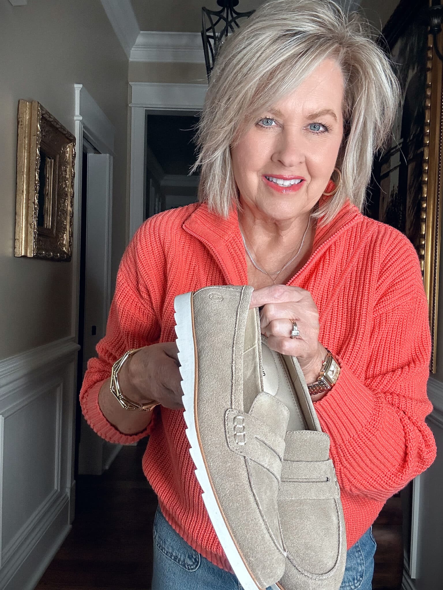 Over 50 Fashion Blogger, Tania Stephens, wearing a bright coral half zip sweater and holding taupe loafers from Lands' End