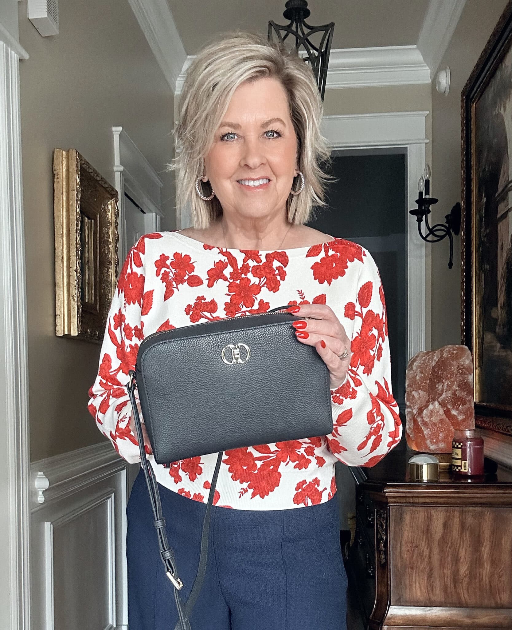 Over 50 fashion blogger, Tania Stephens is wearing a red floral sweater and carrying a navy crossbody bag