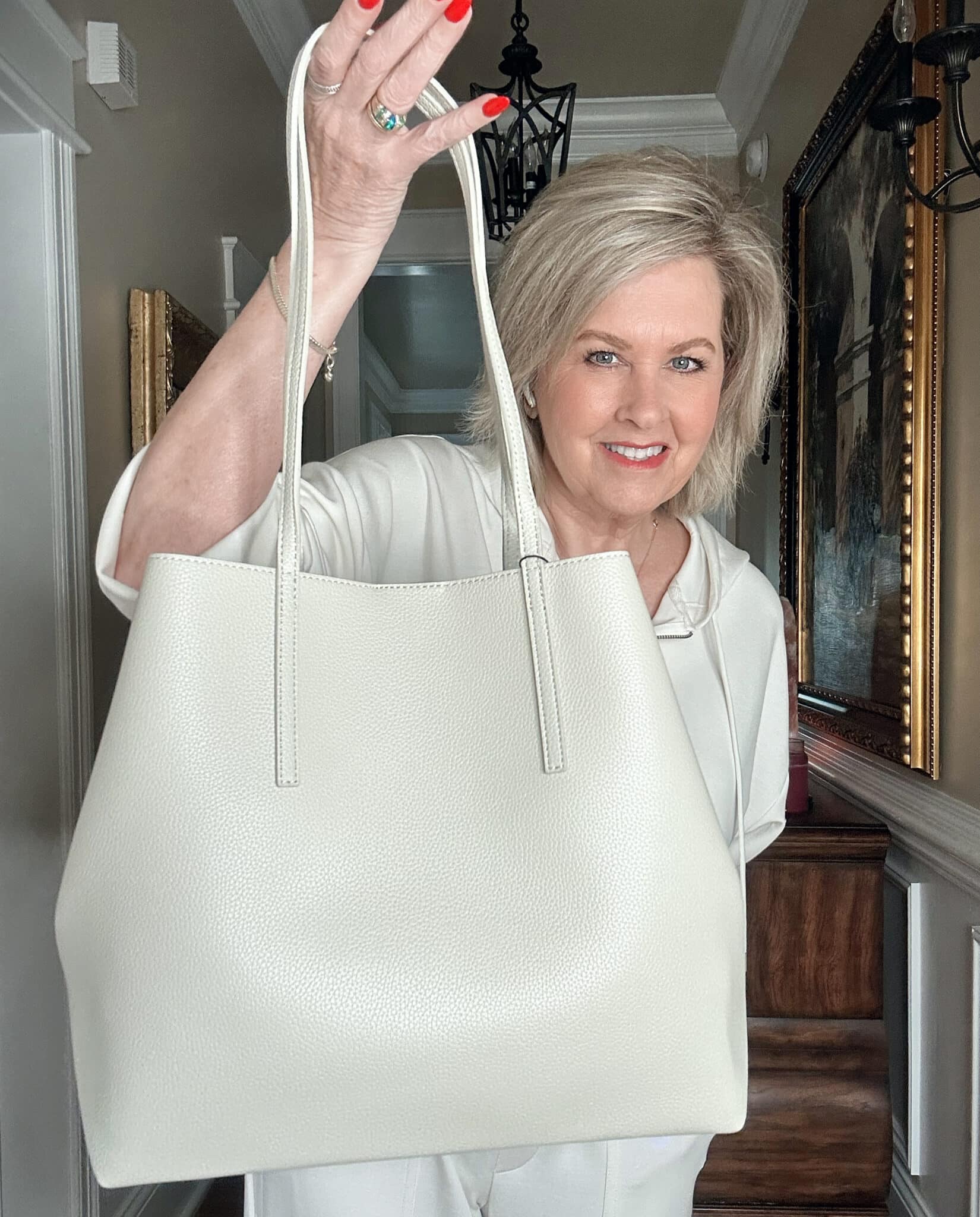 Over 50 Fashion Blogger, Tania Stephens is wearing a neutral outfit consisting of an ivory zip hoodie and ivory handbag