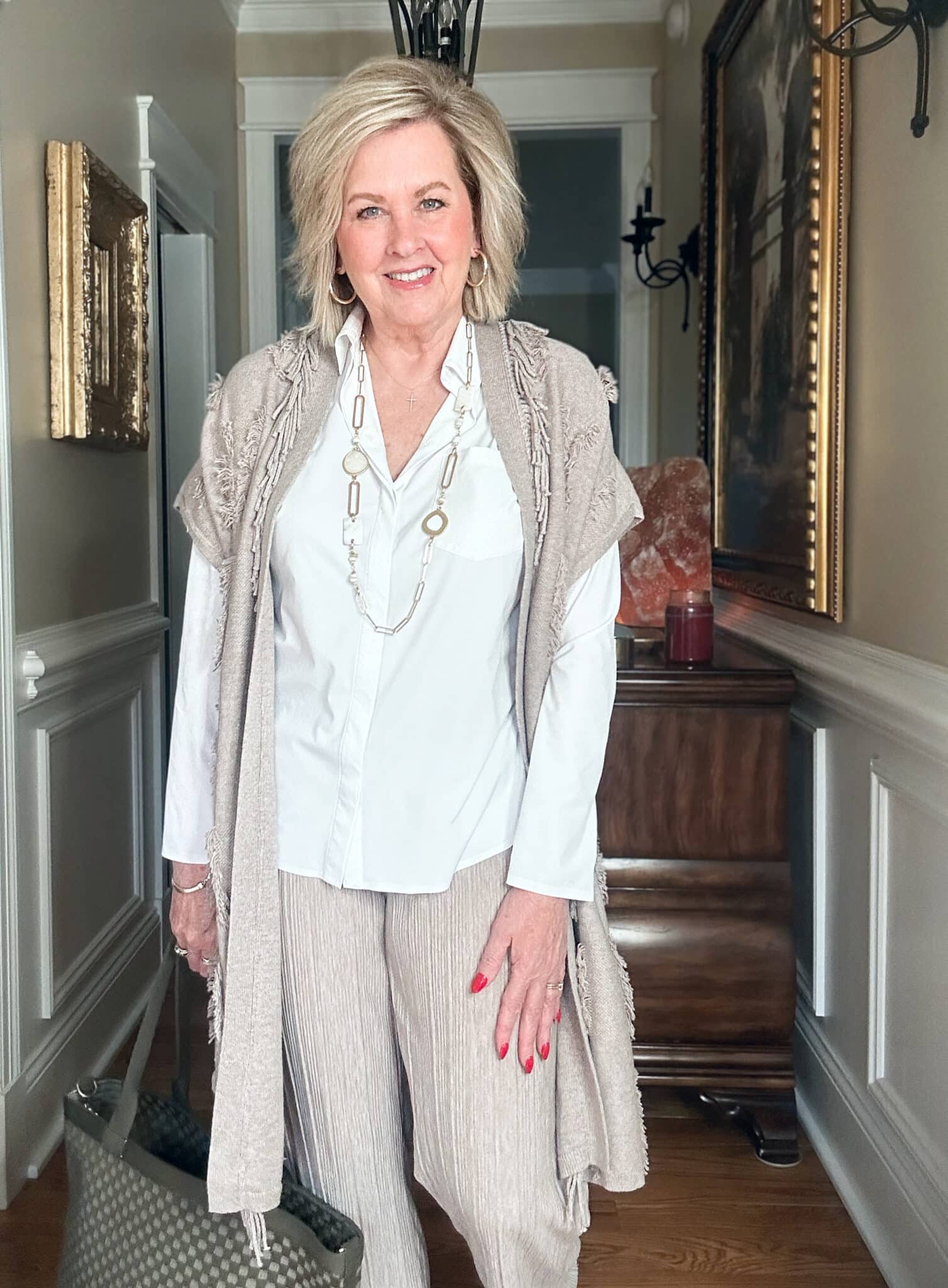 Over 50 Fashion Blogger, Tania Stephens is wearing a neutral outfit consisting of a fringed vest with a white button up shirt