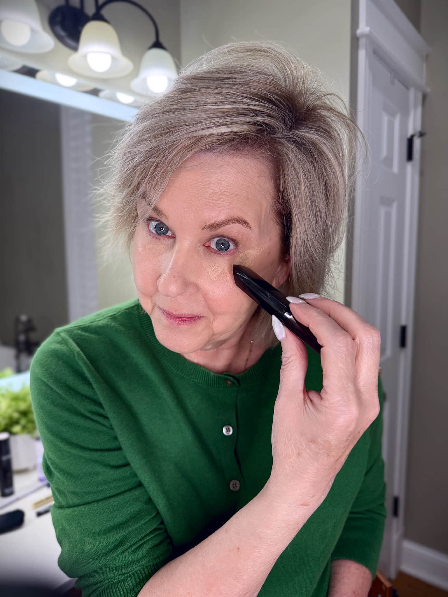Tania Stephens in a green sweater with applying concealer makeup from Nordstrom Beauty