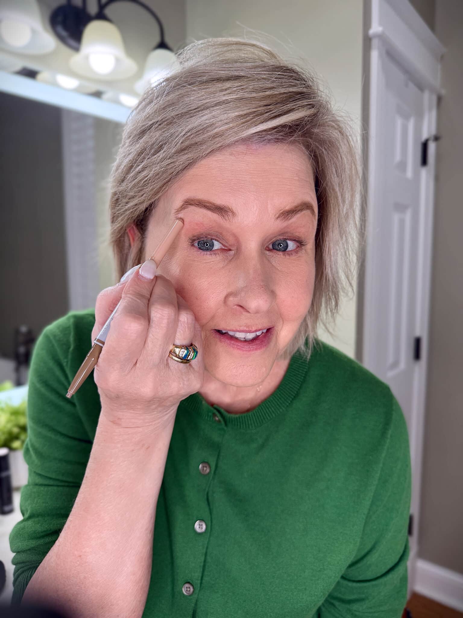 Tania Stephens in a green sweater with applying highlighter to the bows with makeup from Nordstrom Beauty