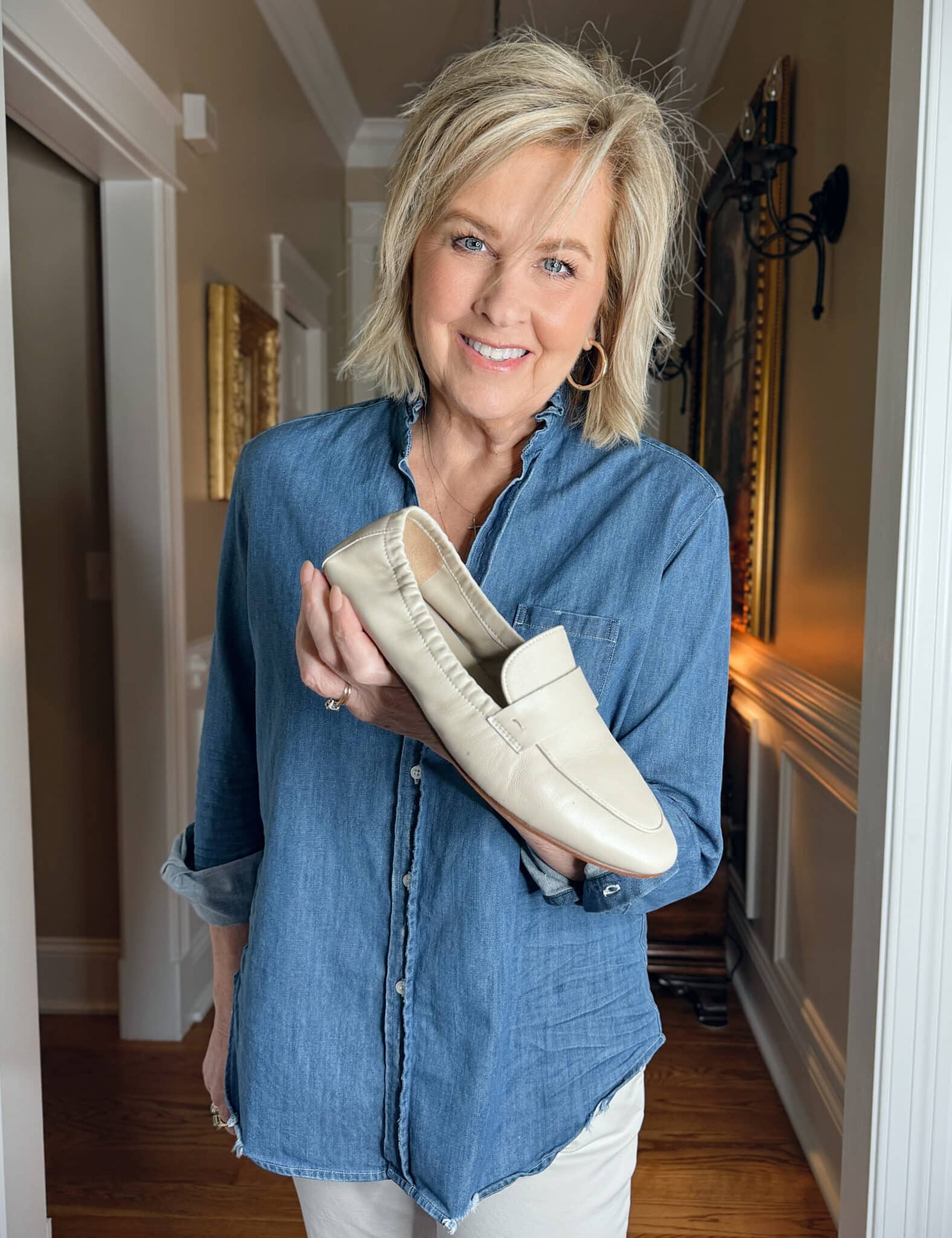 Tania Stephens wearing Frank & Eileen denim button up shirt with ruffle collar and holding a beige loafer 