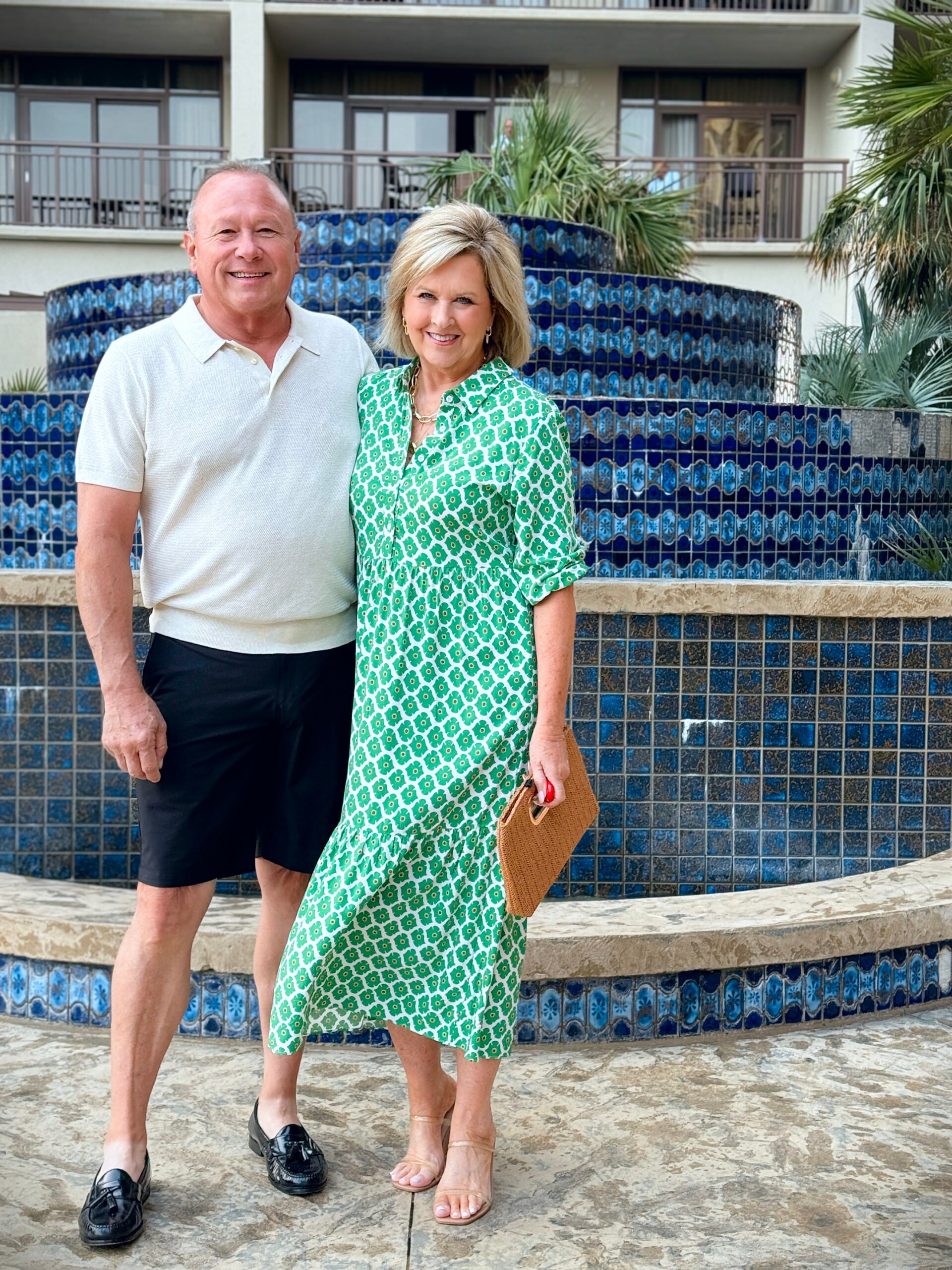 woman over 50 wearing a colorful green dress with a man in black shorts