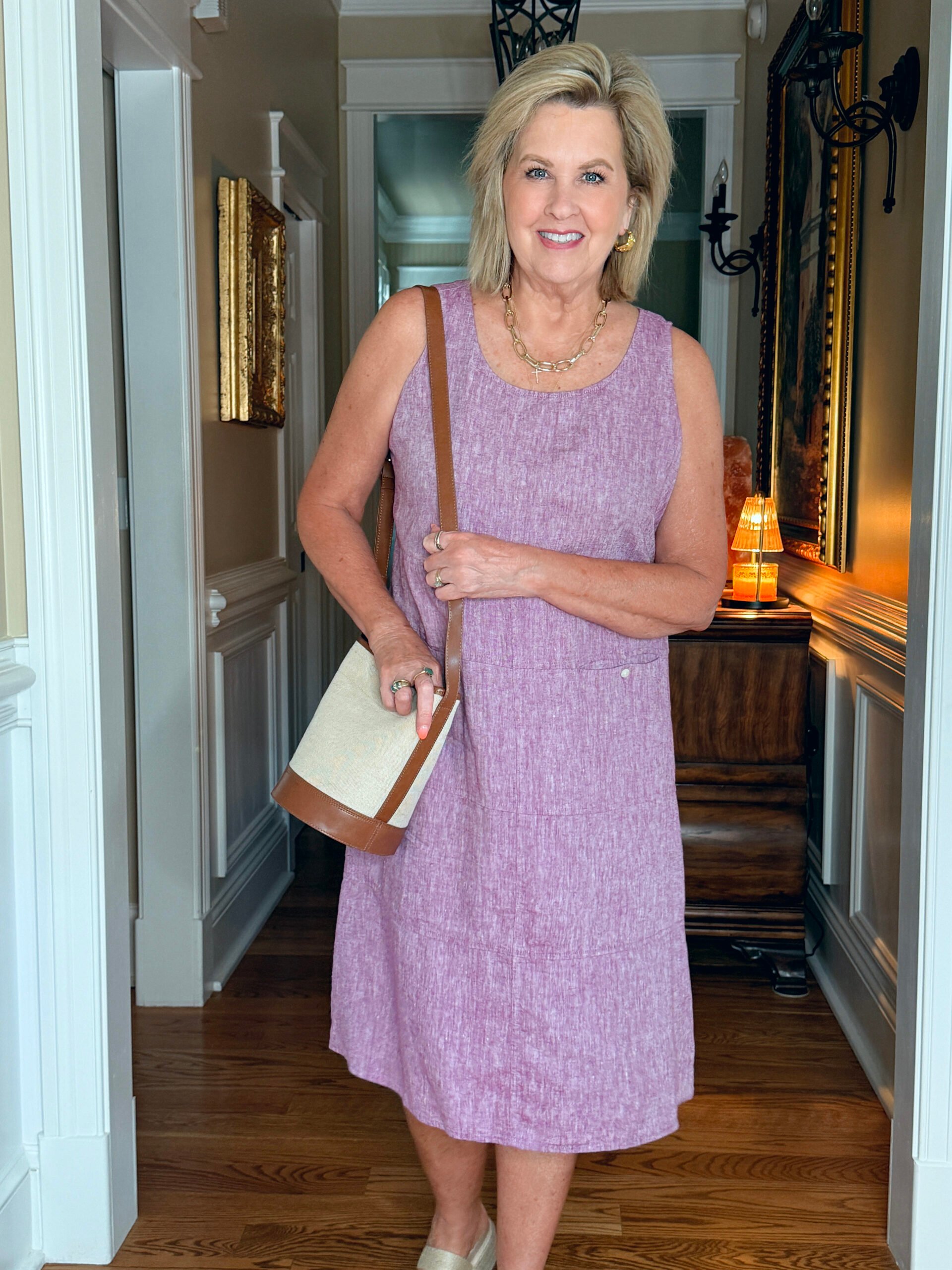 Tania wearing a sleeveless dusty rose linen shift dress with a crossbody bag and gold jewelry