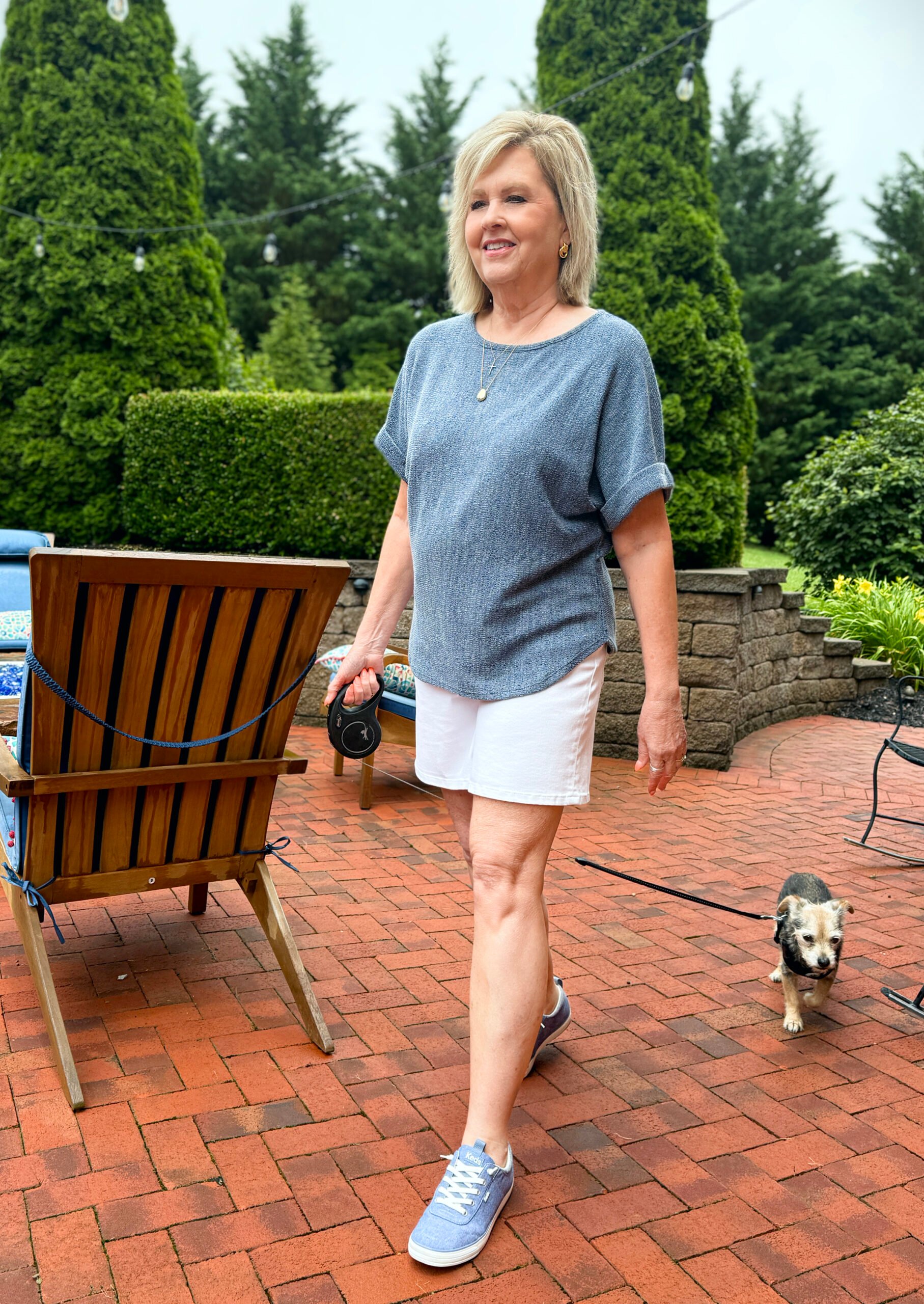 Woman walking dog in chambray slip-on sneakers, white shorts, and a denim-colored top.