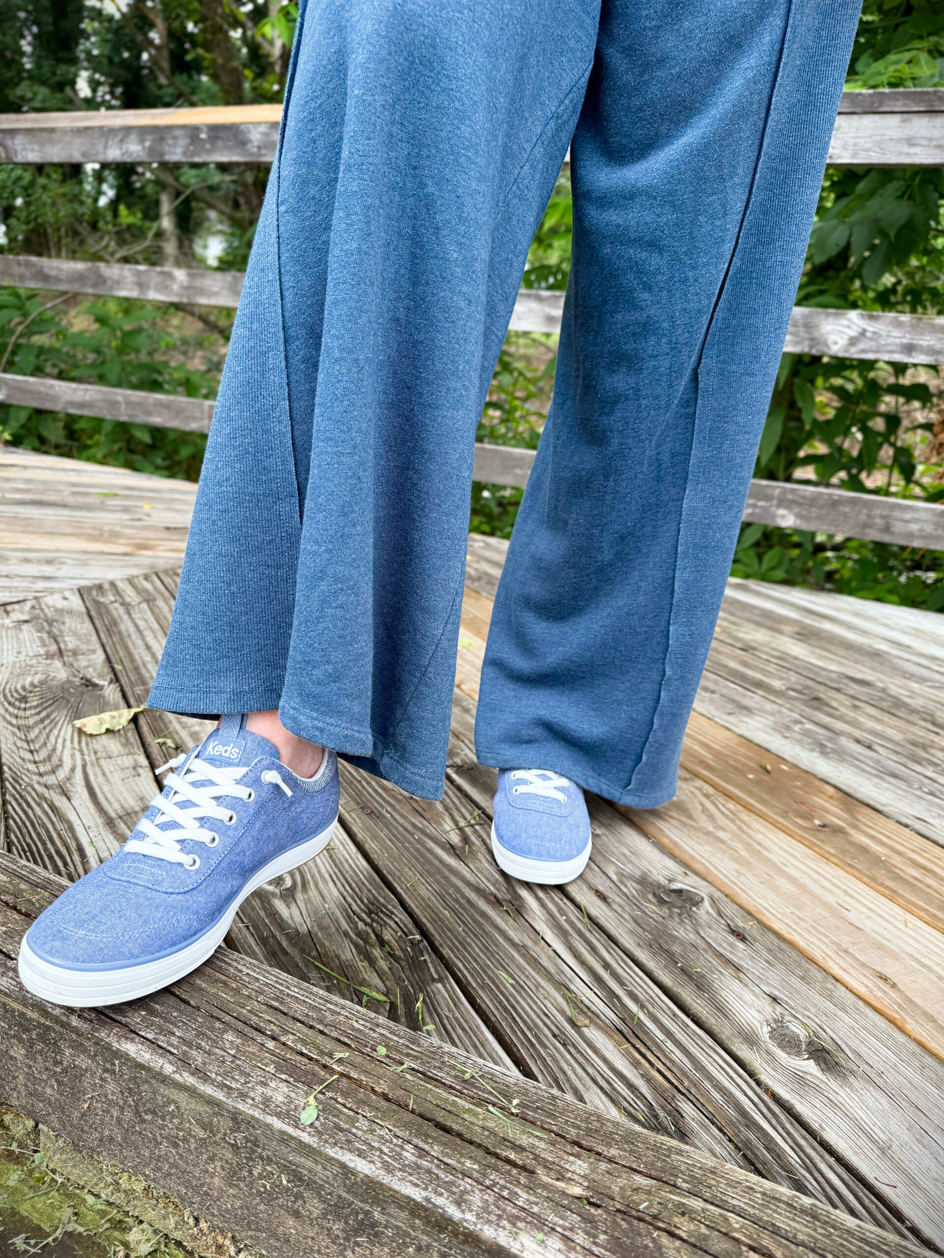 Keds Center III Chambray Slip-On Sneakers with flowy blue pants on a wooden walkway