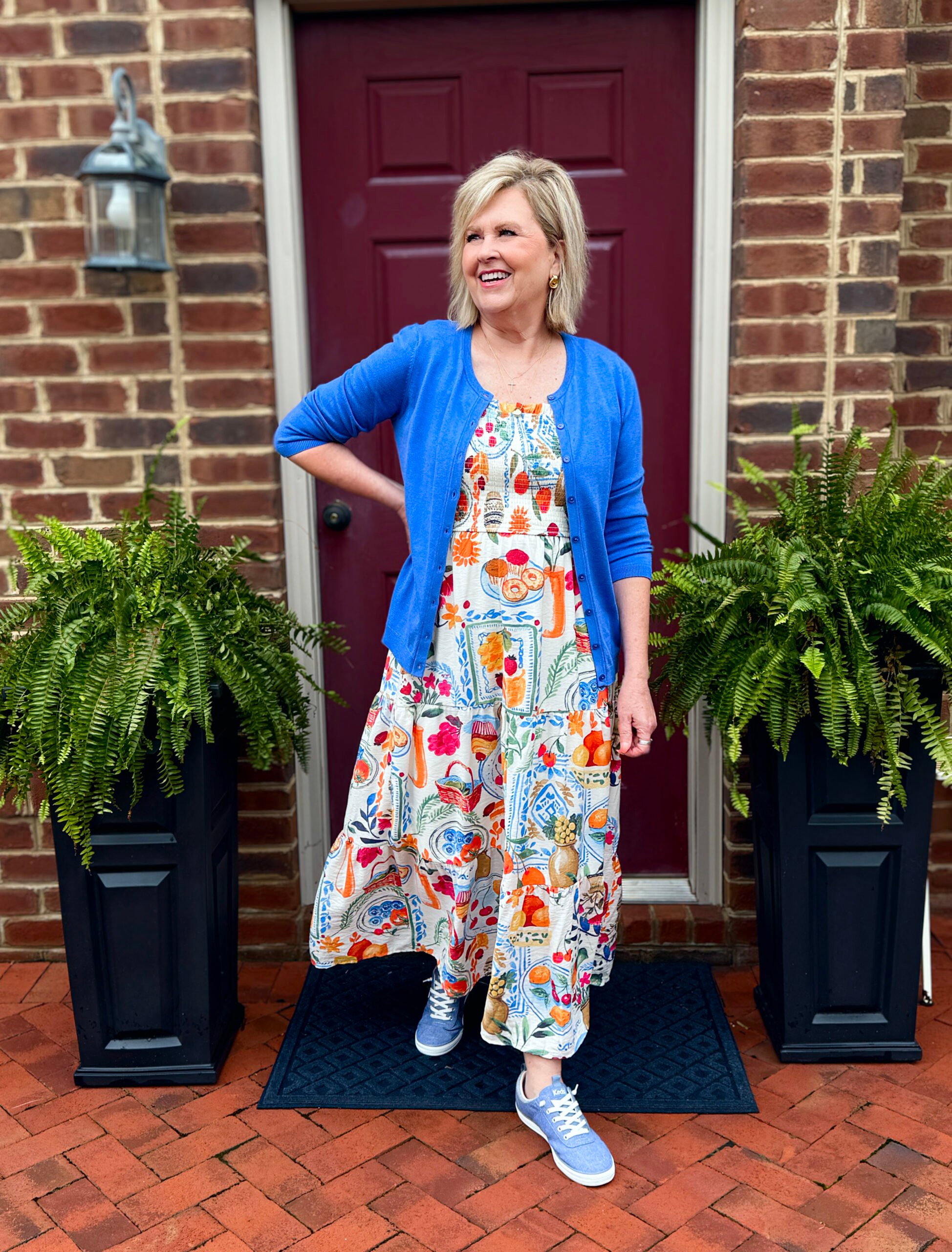 Woman in printed dress, cardigan, and slip-on chambray Keds at a lunch spot.