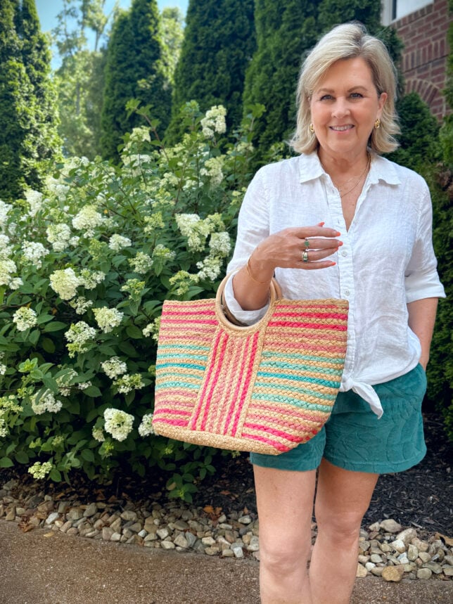 woman in a white shirt and green shorts holding a sriped straw handbag