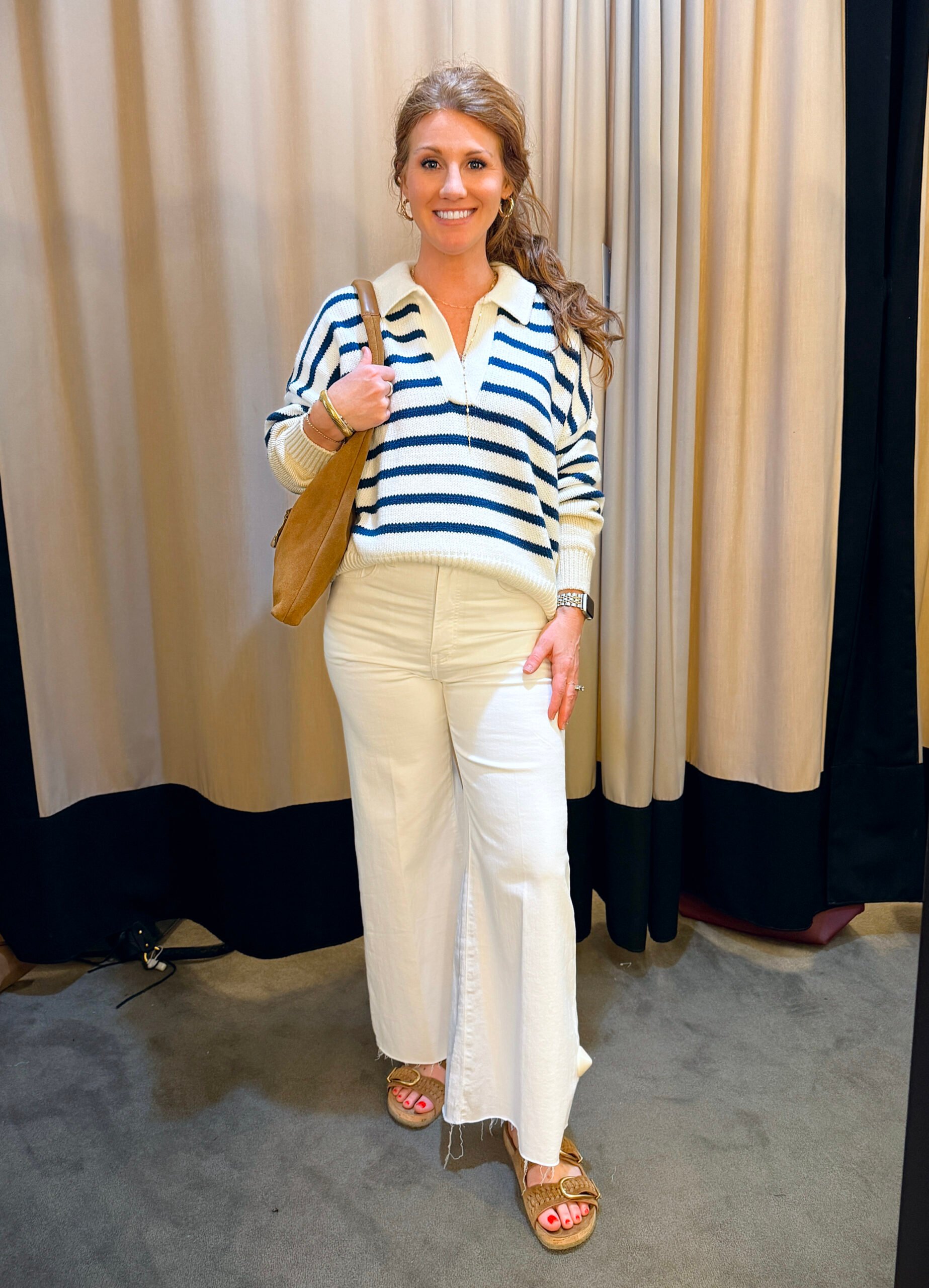 Woman with red hair wearing a navy & white striped sweater with white wide leg jeans