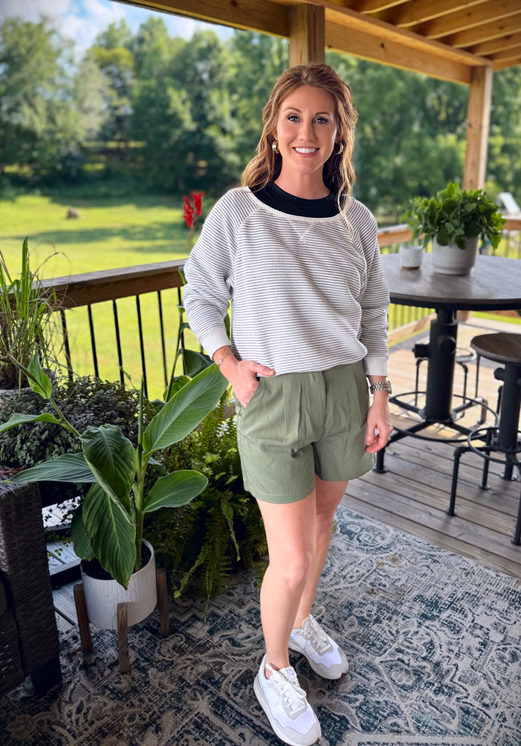 Stephanie, a petite 5'3" tall, wearing olive green shorts from Amazon with a black tee and striped sweater