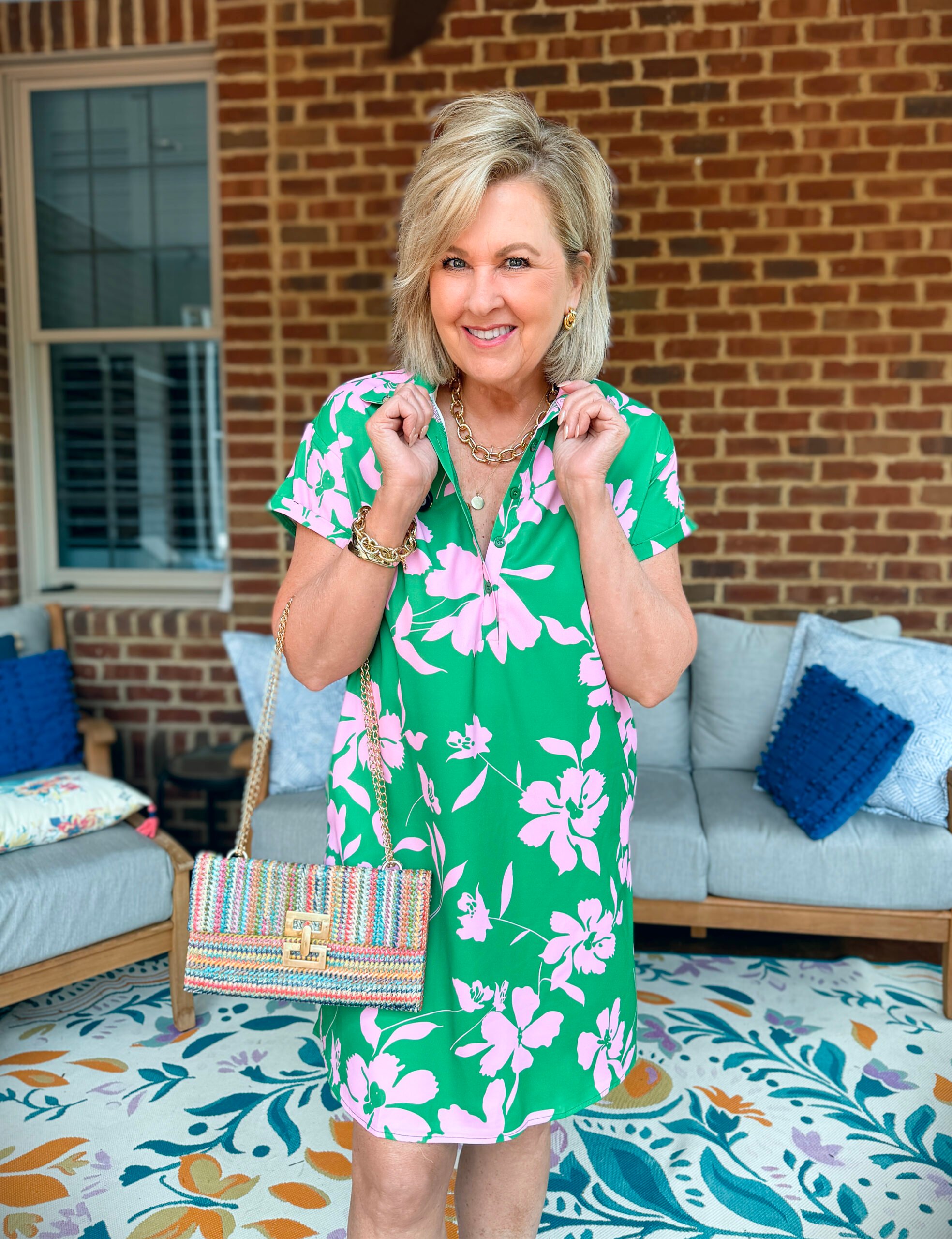 Tania wearing a pink and green short dress from Amazon with gold jewelry and a multi-colored clutch