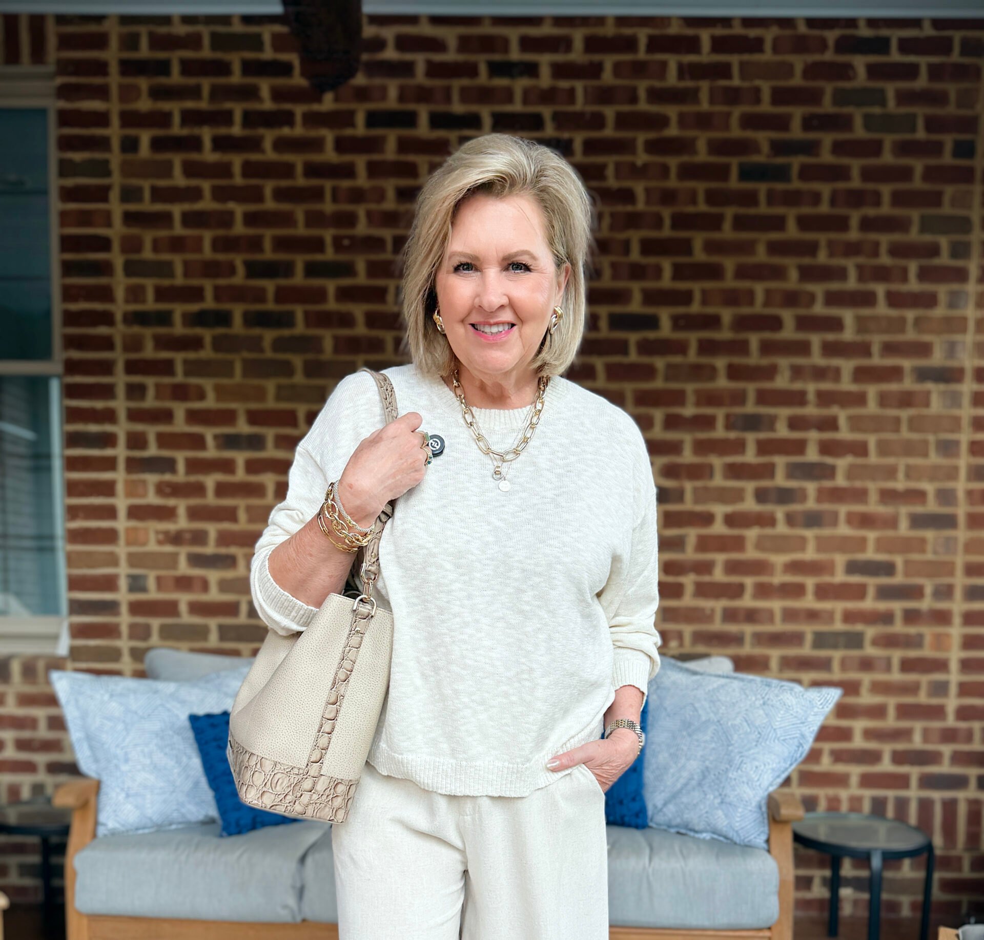 Tania is wearing a beige beach sweater in front of a couch on a porch