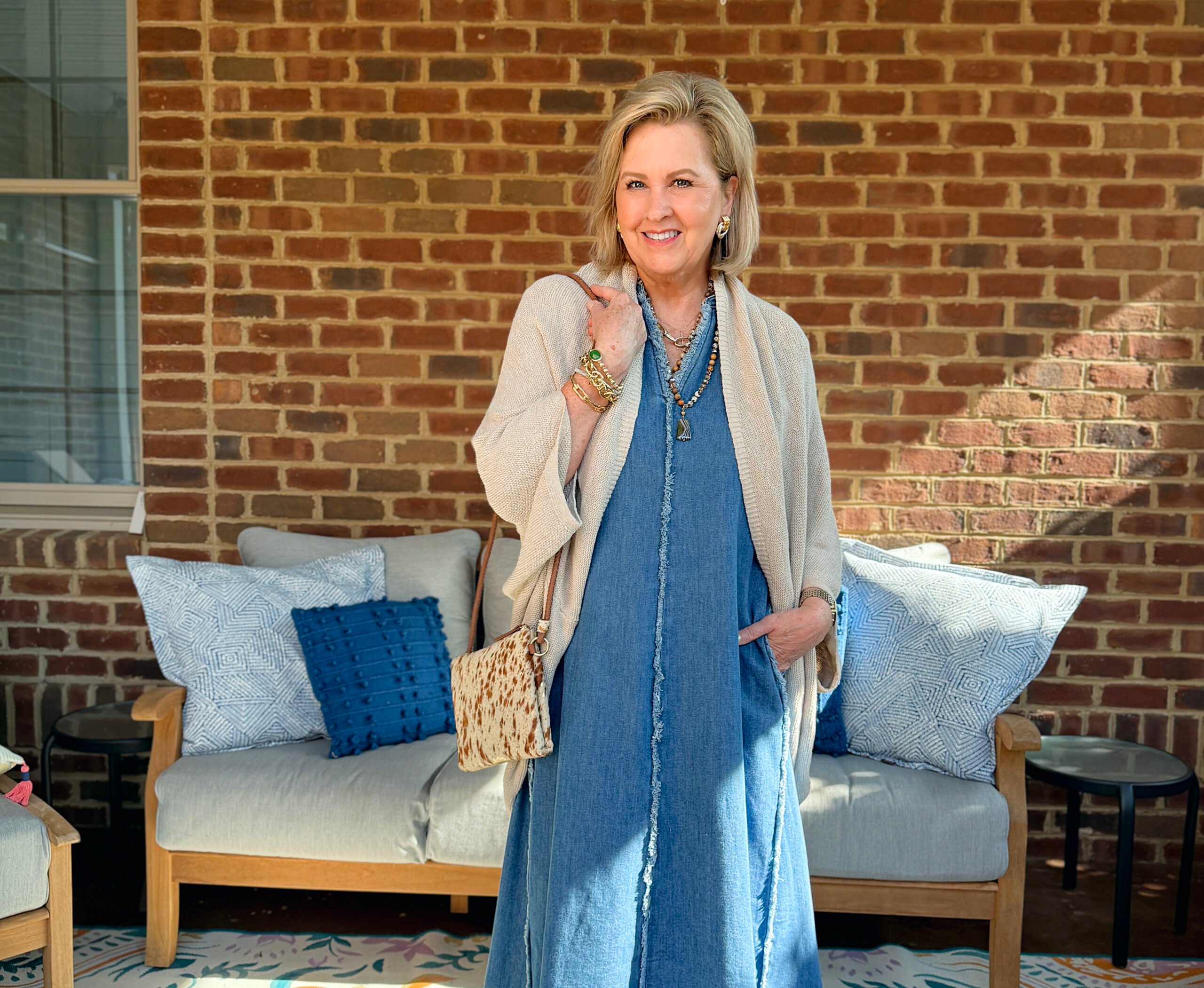Tania is wearing a frayed denim dress with a beige wrap on a brick porch