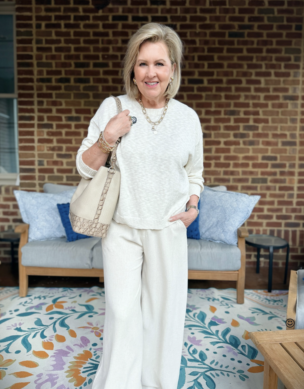 Tania is wearing a beige monochromatic outfit in front of a couch on a porch