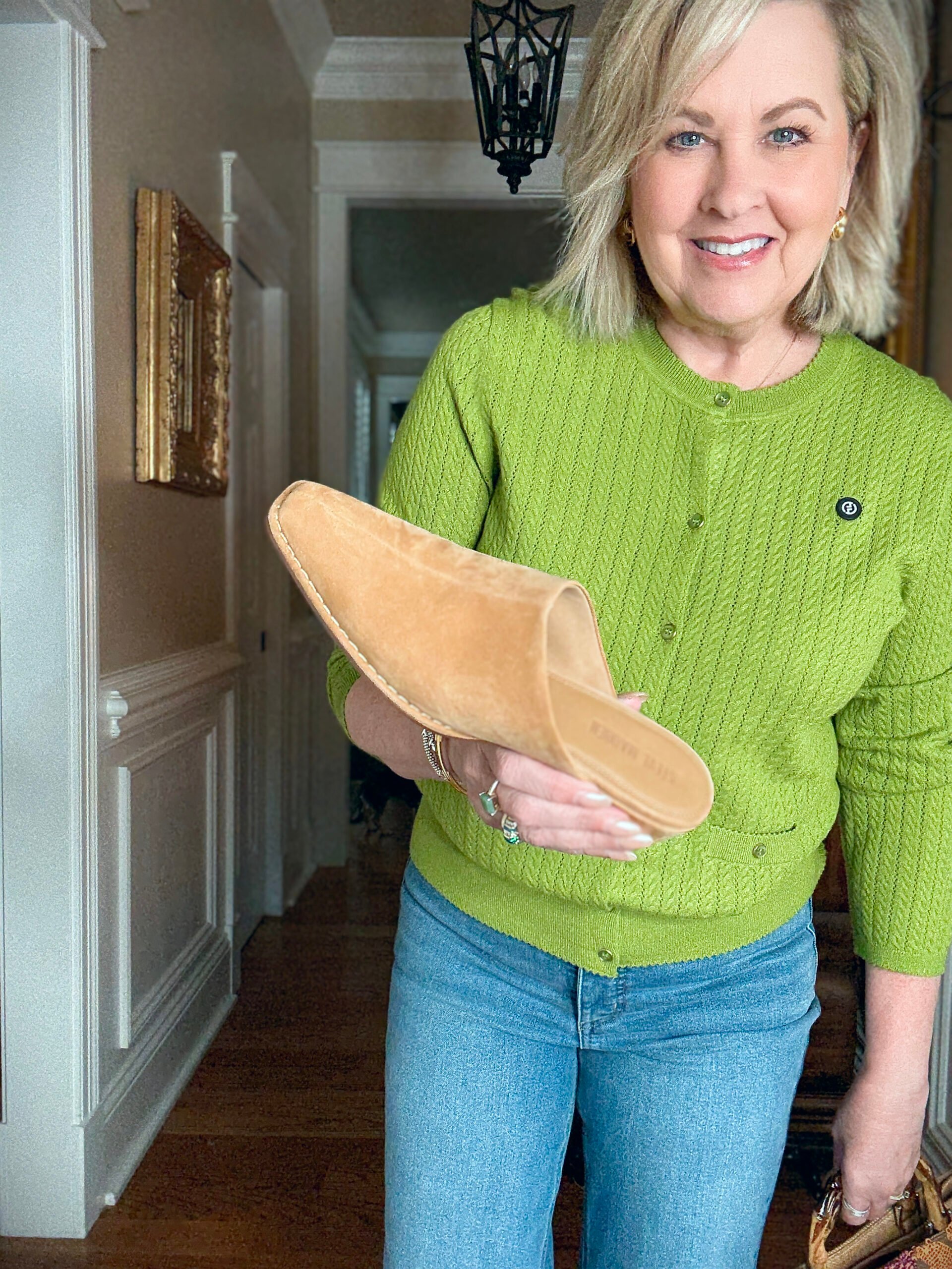 Tania is a green sweater holding a suede mule