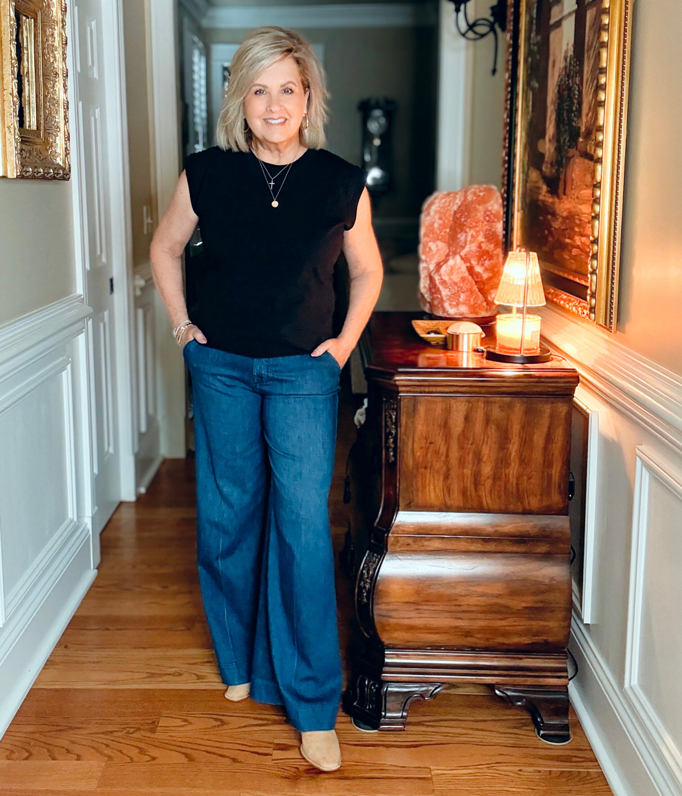 Casual outfit for women over 50 featuring a black muscle tee tucked into wide-leg trousers with mules and layered bracelets