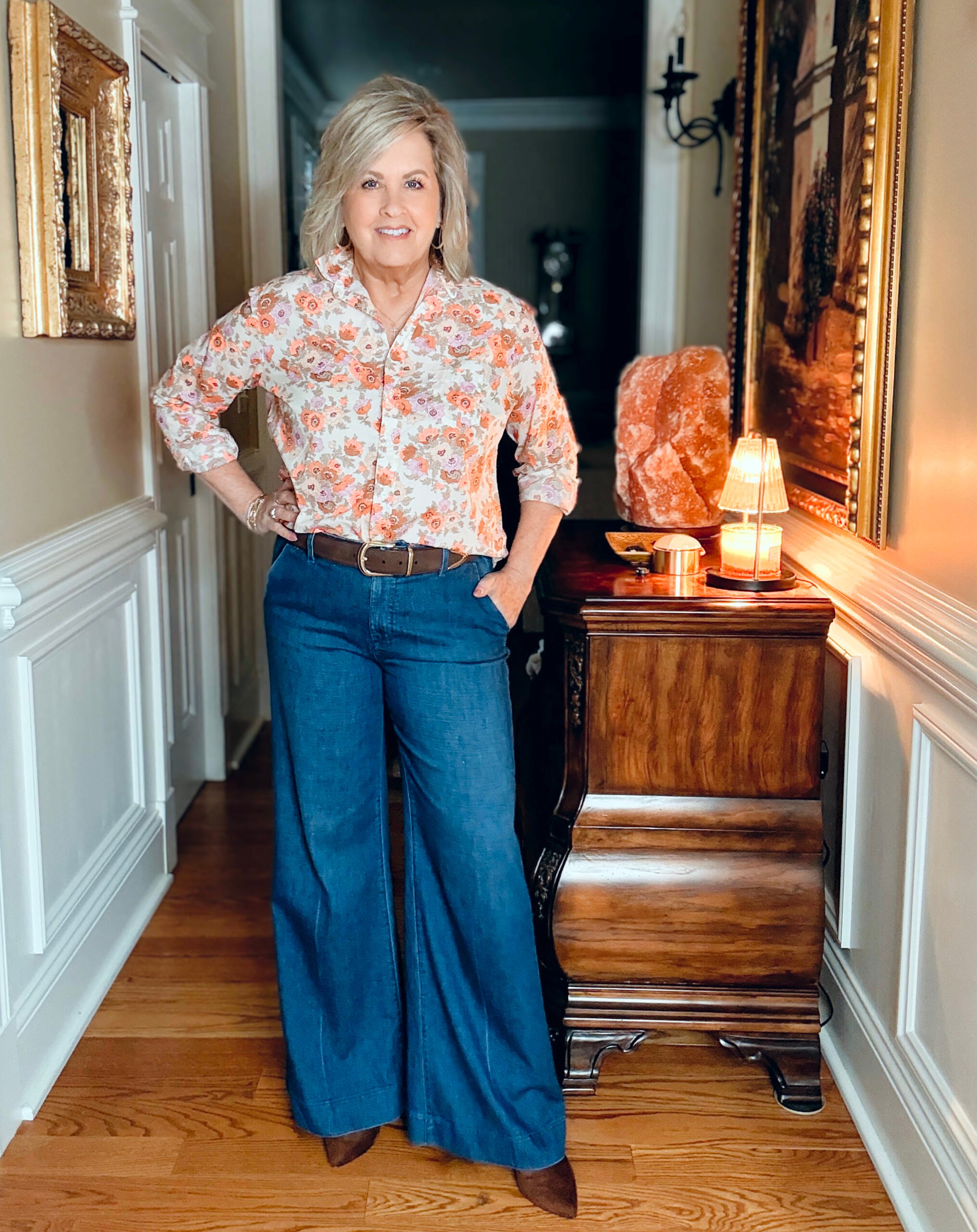 Woman over 50 wearing wide-leg jeans with a relaxed button-up shirt styled with a suede belt and ankle boots for a casual polished fall outfit