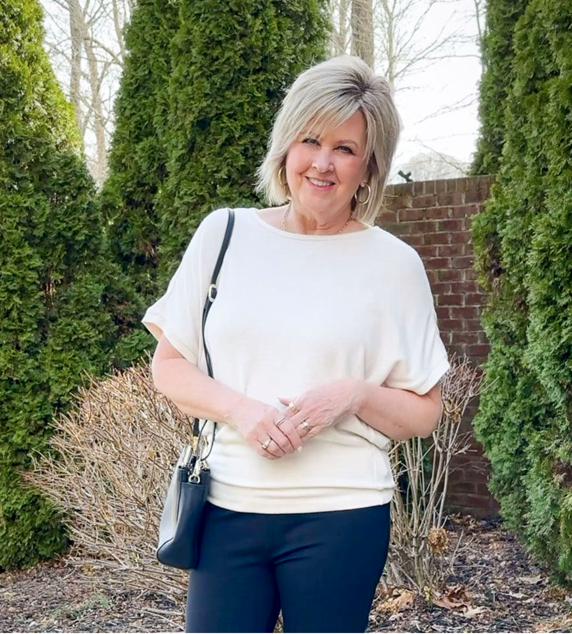 Tania wearing a Quince ivory cashmere dolman sweater for summer in front of a brick wall 