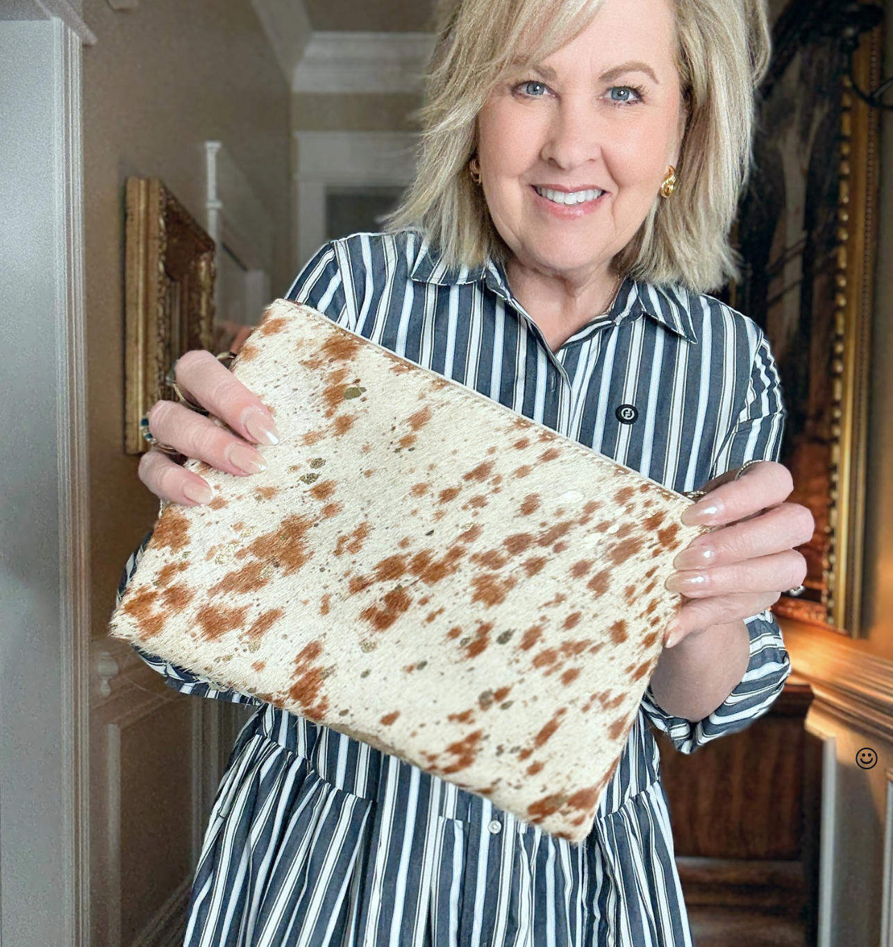 Tania is wearing a striped dress and holding a cow print crossbody from Chicos