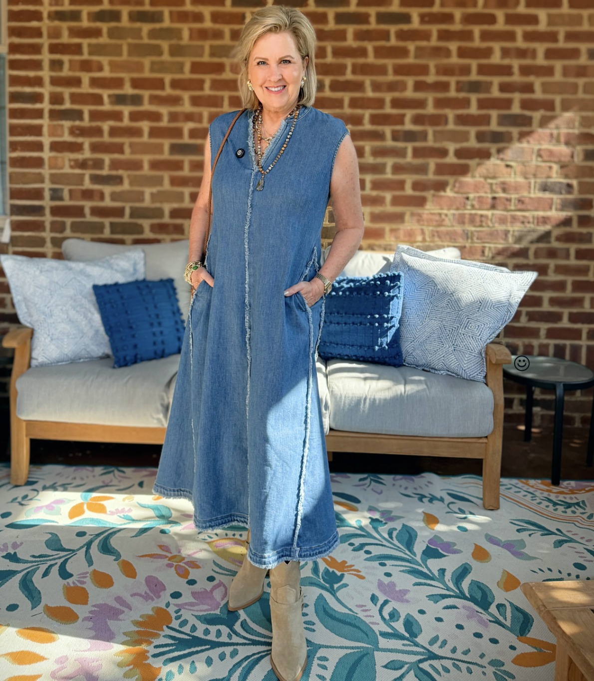 Tania is wearing a frayed denim dress in front of a couch on a porch
